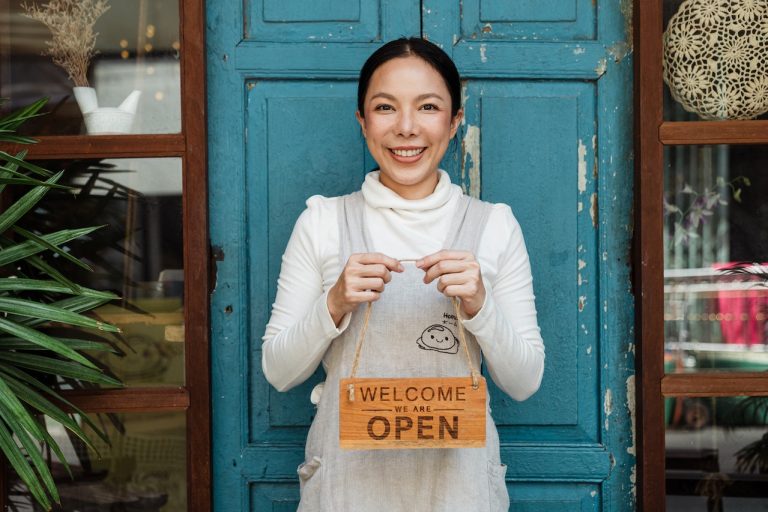 Woman holding welcome open sign in front of door