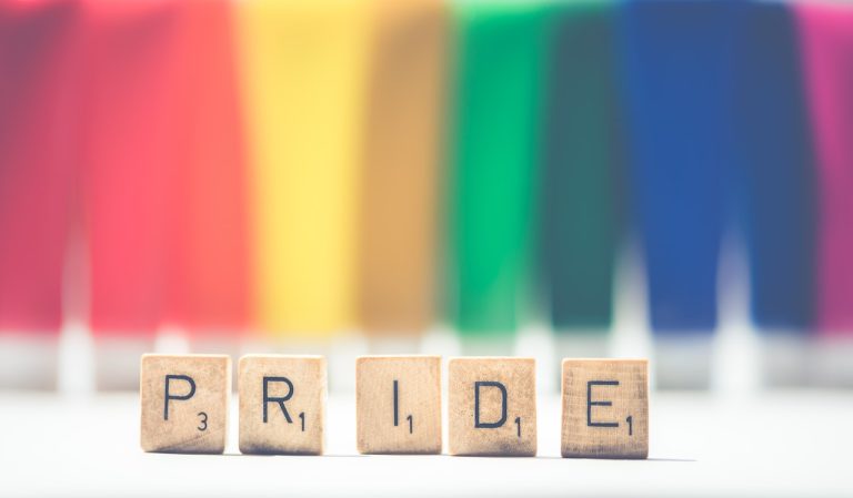 Rainbow background with scrabble letters spelling pride