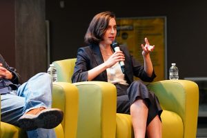 Ava Kofman sitting in a chair, holding a microphone speaking to an audience