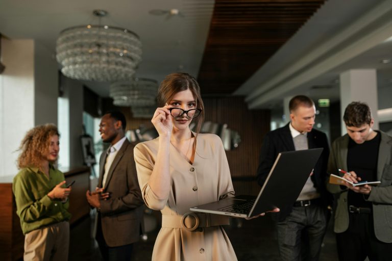 A woman holds a laptop in a room full of people in a return to the office