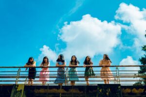 Six girls in dresses leaning against a railing