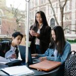 A group of students sits at a table outside exchanging notes.