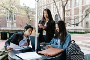 A group of students sits at a table outside exchanging notes.