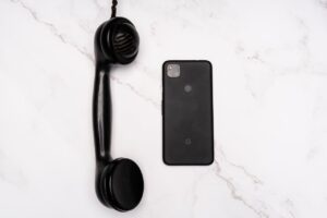Black Cellphone Beside a Black Telephone Receiver