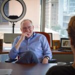 Man in desk chair chatting with another man