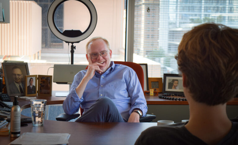 Man in desk chair chatting with another man