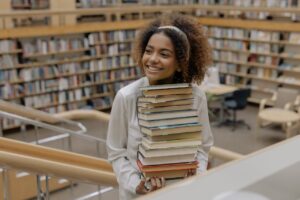 Woman carrying stack of books and smiling