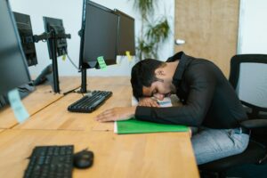 A man sits at his desk with his head on his hands.