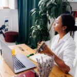 women sitting at desk with computer demonstrating a chart to a phone camera