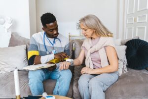 A health aide taking the blood pressure of an elderly woman inside her home.