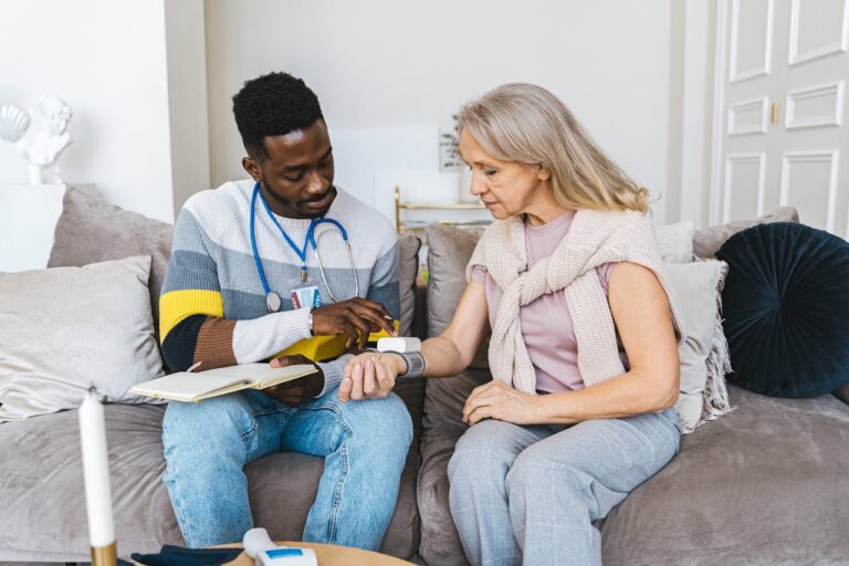 A health aide taking the blood pressure of an elderly woman inside her home.