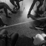 Grayscale of people sitting in a circle only showing their shoes