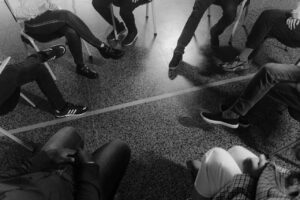 Grayscale of people sitting in a circle only showing their shoes