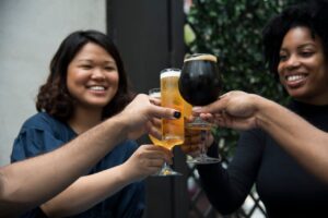Several women clinking beer glasses to cheers as a group