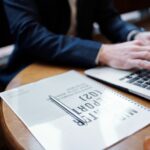 Pen on top of a document next to a man typing on a computer