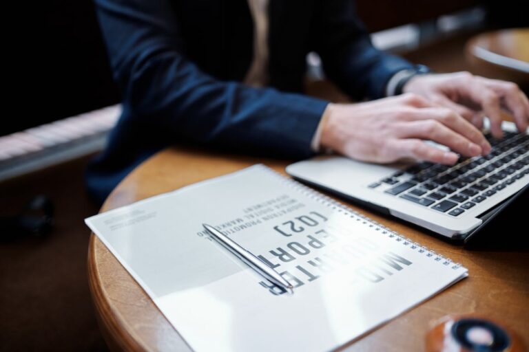 Pen on top of a document next to a man typing on a computer