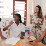 Four women gathered around a table with notebooks and pens, laughing