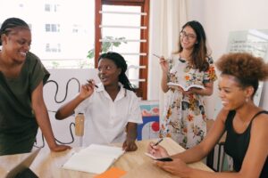 Four women gathered around a table with notebooks and pens, laughing