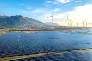 Solar panels and wind turbines with a blue sky and green mountains