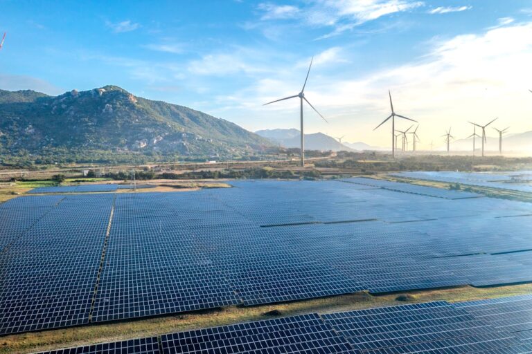 Solar panels and wind turbines with a blue sky and green mountains