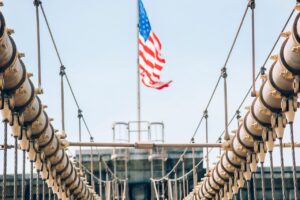 Close-up view of Brooklyn Bridge cables with an American flag waving in the background.