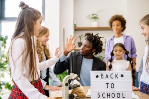 Teacher and students in classroom sharing a high five, symbolizing teamwork and diversity.